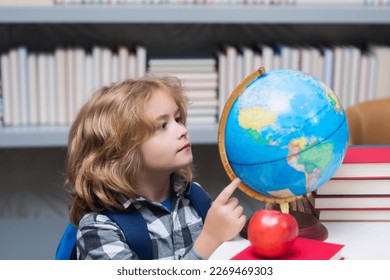 Pupil looking at globe in library at the elementary school. Nerd school kid. Clever child from elementary school with book. Smart genius intelligence kid ready to learn. World globe.