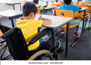 A Pupil In Wheel Chair Working At His Desk At School