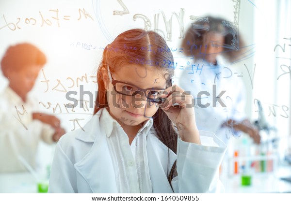 Pupils girl writing physics formula on glass\
board in laboratory science at\
school.