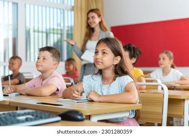 Pupils sitting in classroom during lesson. Female teacher standing behind.