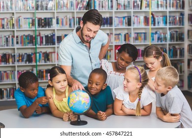 Pupils and teacher looking at globe in library at elementary school