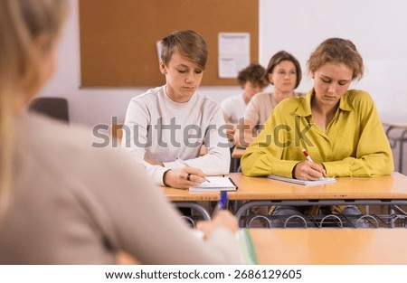 Pupils write in notebooks while sitting at desks in a school class
