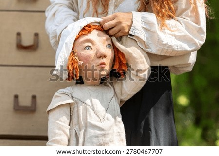 Puppet master manipulating a handmade doll with red hair and a linen bonnet