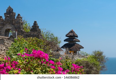 Pura Luhur Uluwatu Temple, Bali on cliffs above blue tropical sea with pink flowers on front 