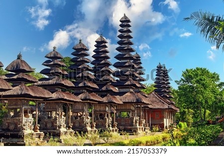 Pura Taman Ayun Temple, Bali - View on traditional meru towers in a row of balinese hindu temple with multiple thatched roofs , blue summer sky, green trees 