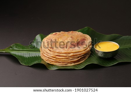 Puran Poli, also known as Holige, is an Indian sweet flatbread from India consumed mostly during Holi festival. Served on banana leaf with pure Ghee over black background.