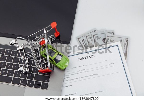 Purchase contract for a car with laptop, money and\
toy car in a shopping\
cart
