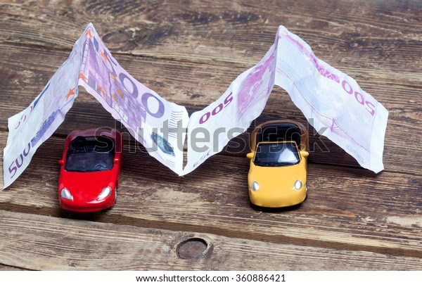 purchase, sale or car
insurance.metaphor.Two little toy cars covered with paper money on
a wooden surface