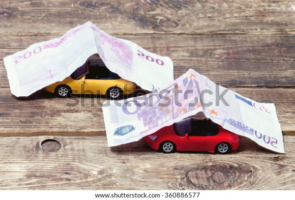 purchase, sale or\
car insurance.metaphor.Two little toy cars covered with paper money\
on a wooden\
surface.toned