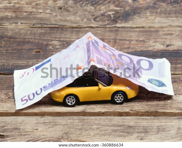 purchase, sale or car\
insurance.metaphor. little toy car covered with paper money on a\
wooden\
surface.toned\
