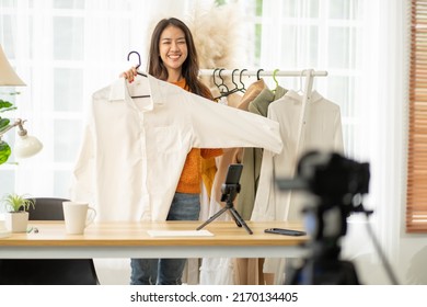 Purchase Shopping And Remote Buying Concept.Asian Beautiful Female Sell Cloth Product Online Live Streaming At Home.Young Woman Use Mobile Phone Video Call Shows Goods To Customer And Present Detail.