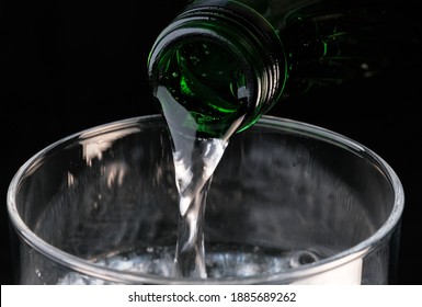 Pure Carbonated Water Pouring From A Bottle Into A Transparent Glass On A Black Background Close-up Macro Photography