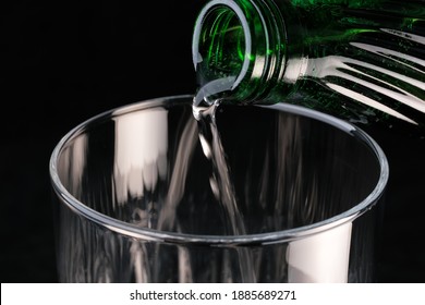 Pure Carbonated Water Pouring From A Bottle Into A Transparent Glass On A Black Background Close-up Macro Photography