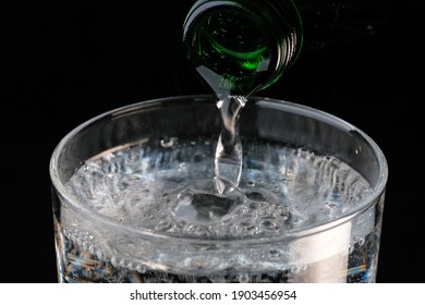 Pure Carbonated Water Pouring From A Bottle Into A Transparent Glass On A Black Background Close-up Macro Photography