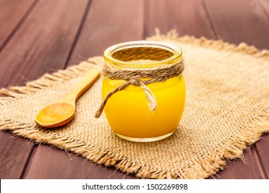 Pure or desi ghee (ghi), clarified melted butter. Healthy fats bulletproof diet concept or paleo style plan. Glass jar, wooden spoon on vintage sackcloth. Wooden boards background, copy space close up