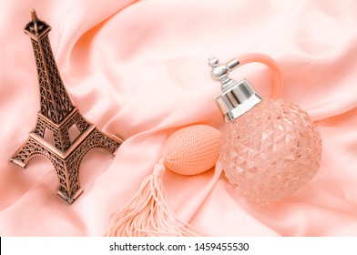 Pure Essence Perfumes, Fragrance Of France And Romantic Mood In Paris Concept Theme With A Vintage Bottle Of French Perfume On Pink Silky Satin Or Silk Next To Miniature Replica Of The Eiffel Tower