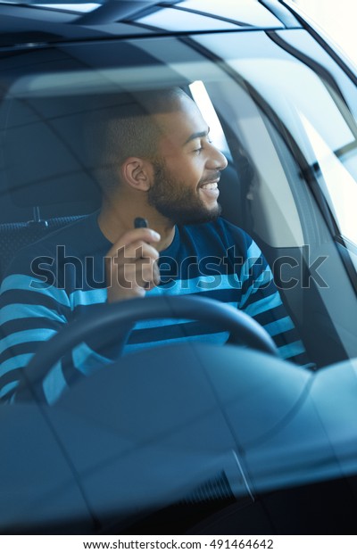 Pure happiness.\
Vertical shot of a happy African man sitting in his new car holding\
car keys looking away\
smiling