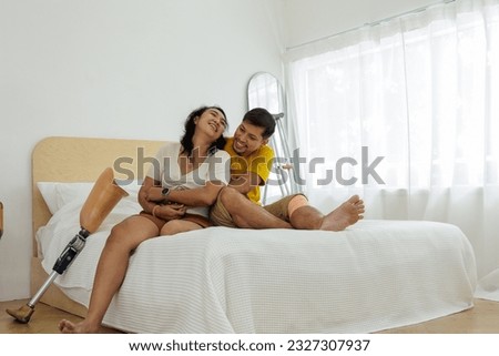 The pure joy and love between two Asian young adults with leg disabilities. They are smiling, laughing, and embracing each other in the comfort of their bedroom, radiating happiness and warmth