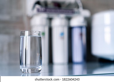 Pure water in glass and water filters on the blurred background. Household filtration system.