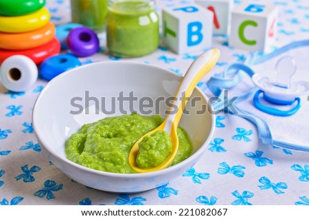 Puree of green in the small bowl is on the background of childrens toys