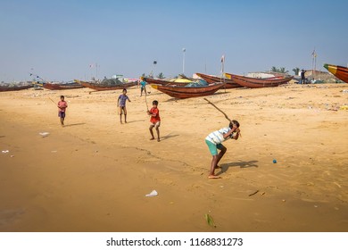 Puri, India - Circa January, 2018. Kids Playing Cricket On The Sandy Beach With Fishing Boats On The Background.