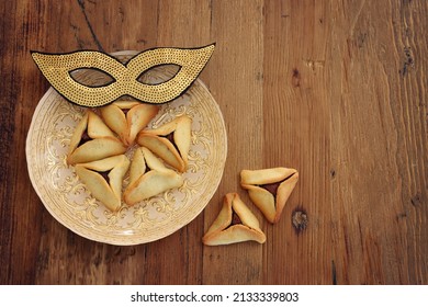 Purim celebration concept (jewish carnival holiday). Hamantaschen cookies and gold carnival mask over wooden background