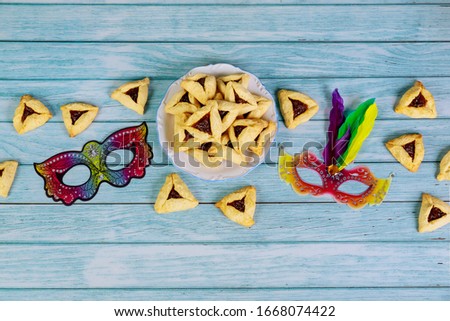 Purim mask and triangle cookies on white wooden background.