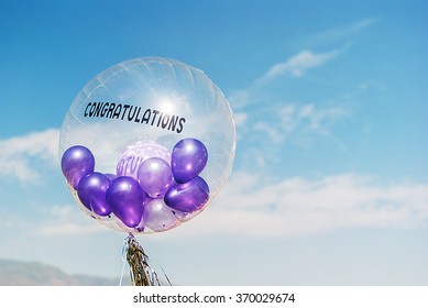 Purple Balloons In Big Balloon Congratulations On Blue Sky With Fluffy Cloud