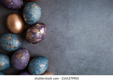 Purple, blue and golden eggs on a dark concrete background. The purple hue trend of 2022 is very peri. Easter card with a copy of the place for the text. Natural dye karkade tea. Top view.
