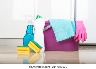 Purple Bucket With Cleaning Products And Pink Gloves In The Room.