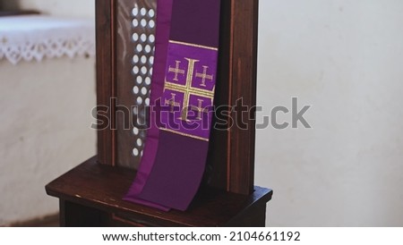 Purple Catholic Priest Stole with Embroidered Jerusalem Cross Hanging Over Grate of Simple Church Confessional