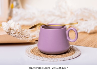 Purple cup with coffee with gold spoon on a white table with flowers next to it and boho style decorations - Powered by Shutterstock