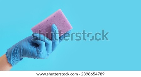 Purple dishwashing sponge in a woman's hand on a blue background. A hand in a latex blue glove holds a sponge for wet cleaning. Professional cleaning. Copy space