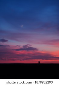 Purple dusk sky with a moon behind the clouds and a silhouette of chimney