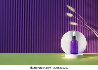 Purple glass dropper bottle with metallic lid on the white podium. Green and violet background with dry plants. Mockup background with cocncrete circle and copy space. Stage with product presentation.