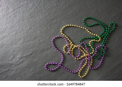 Purple, Green And Gold Mardi Gras Beads On A Gray Slate Table With Copy Space; Landscape View