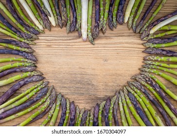 Purple, Green And White Asparagus In Heart Shape On A Rustic Wooden Bachground.