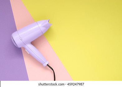 Purple hair dryer on purpe, pink and yellow paper background