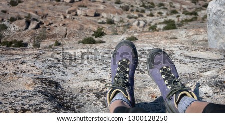 Purple hiker's boot hanging over rocky ledge with giant stone filled valley below