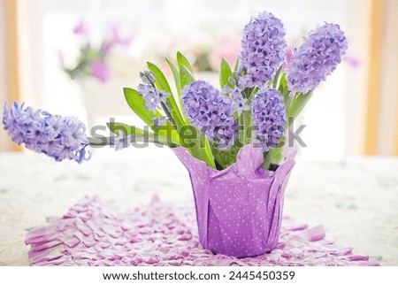 Purple hyacinth flowers in a decorative vase on a table with petals and blurred background.