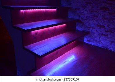 Purple Illuminated Wooden Stairs And Rough Stone Wall