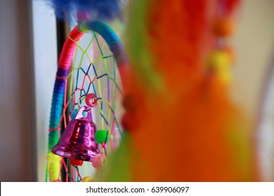 Purple Metallic Bell Next To Orange, Green And Yellow Dream Weaver Feather Design Hanging In Window