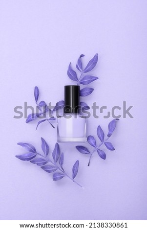 Purple nail polish bottle decorated with leaves on a purple background. Purple nail polish theme.
