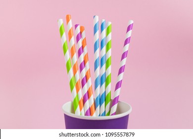 Purple paper cup with colorful paper straws on pink pastel background. Set for a birthday.