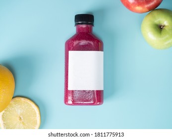 Purple Pastel Color Drink In Plastic Bottle Container With Empty Logo Label. Mixed Many Vegetables And Fruits Smoothie Juice On Studio Background. Lime, Green Apple, Red Apple Decorated.