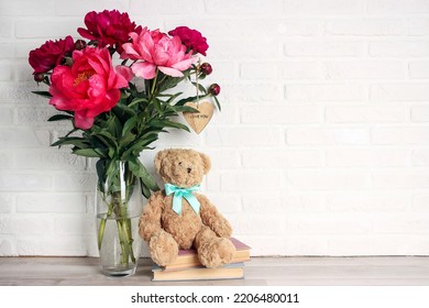Purple peony flowers bouquet with toy bear and books on white brick wall. Copy space for text.  - Shutterstock ID 2206480011