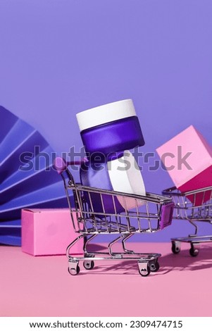 Purple and pink background,  Toy cart with cosmetics, buying cosmetic products in the store. Purple glass cream jar. Pop art cosmetics concept. Cosmetic accessories. Cosmetics mock up.Cream pot.Clean.