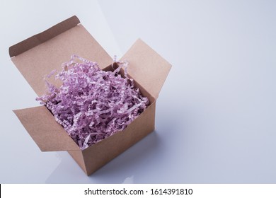 Purple pink shredded paper gifting stuffing cardboard box. White isolated background.