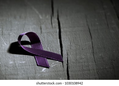 a purple ribbon for the awareness about the unacceptability of the violence against women, on a dark gray rustic wooden surface