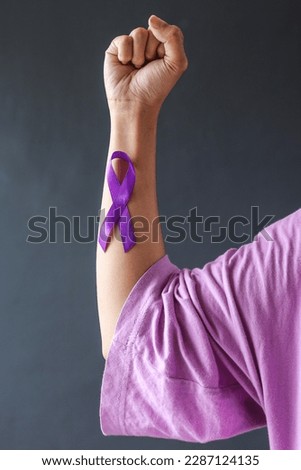 Purple ribbon cancer awareness stick to strong hand close up. World cancer day on a purple colored background. Symbol of Domestic Violence Awareness, Epilepsy Awareness. 